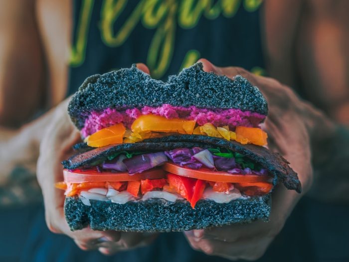 Person holding a vibrant vegan sandwich with colourful vegetables and black bread