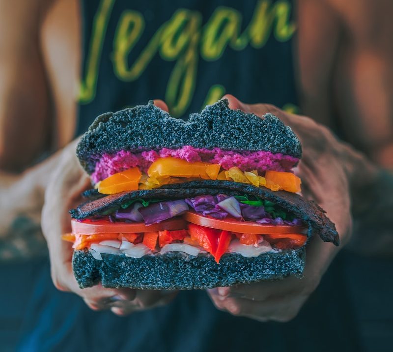 Person holding a vibrant vegan sandwich with colourful vegetables and black bread
