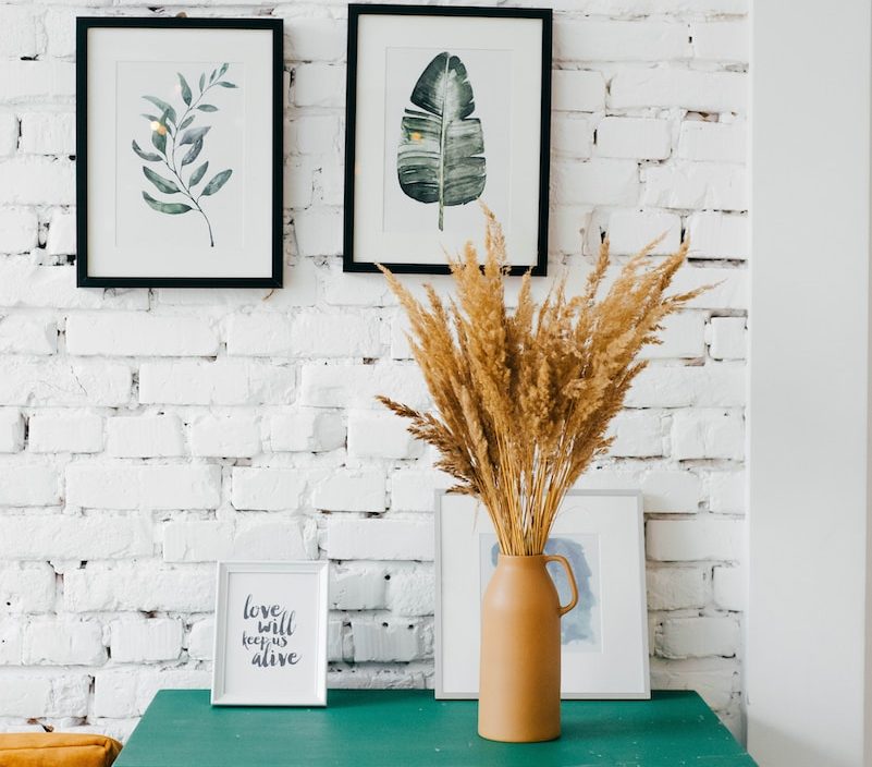 Cosy room with botanical art, green dresser and wheat vase against white brick wall